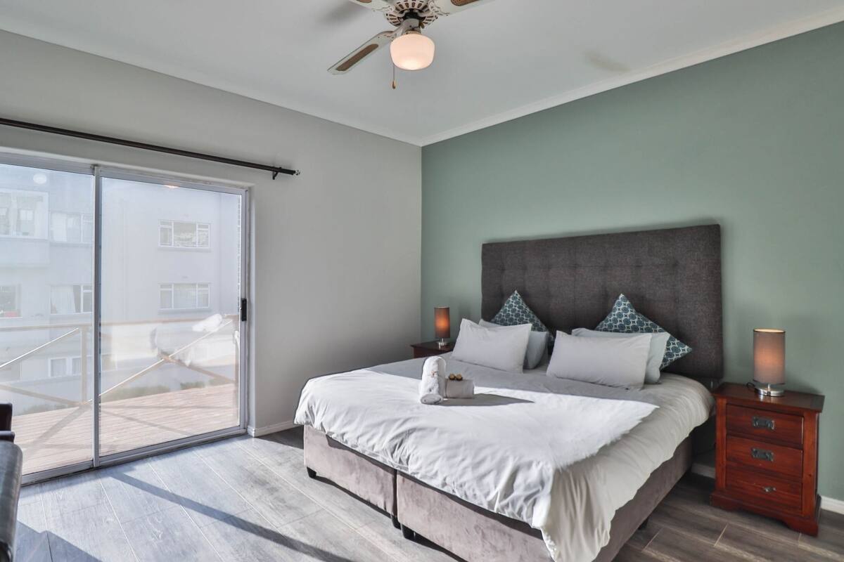 A bedroom with a large bed, a ceiling fan, a nightstand, and a sliding glass door leading to an outdoor area.