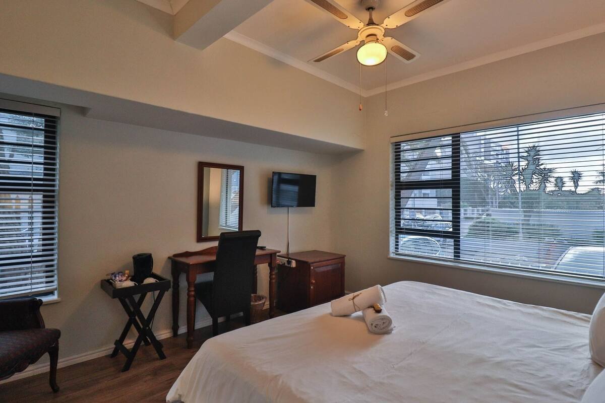 A hotel room with a bed, desk, chair, TV, and large windows.