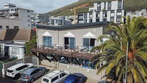 Un edificio moderno con terraza en la azotea, zona de estacionamiento privado y una grúa de construcción al fondo.