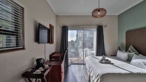 Habitación de hotel con cama, escritorio con cafetera, televisión y balcón con vistas.