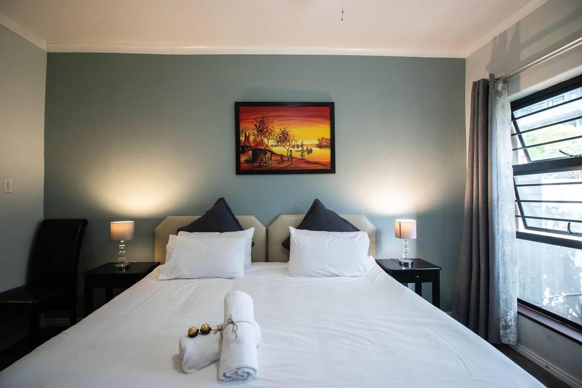 A hotel room with a large bed, two bedside tables with lamps, a painting on the wall, and a window with curtains.