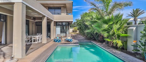 A modern pool area with a rectangular pool, lounge chairs, and a patio with a wooden deck.