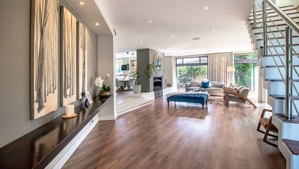 Un vaste espace de vie doté d’un parquet en bois foncé, d’un canapé bleu et d’un escalier avec une rampe en métal.