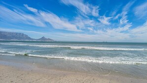 Une plage avec des vagues, un ciel dégagé et des montagnes à l’horizon.