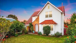 Une maison à deux étages, avec un toit recouvert de tuiles rouges, un porche à l’avant et un jardin bien entretenu.