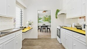 Une cuisine étroite avec des meubles blancs, un plan de travail jaune et un coin repas comprenant une table et des chaises.