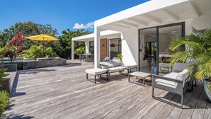 Un patio exterior moderno con cubierta de madera, sillones blancos y un paraguas amarillo.