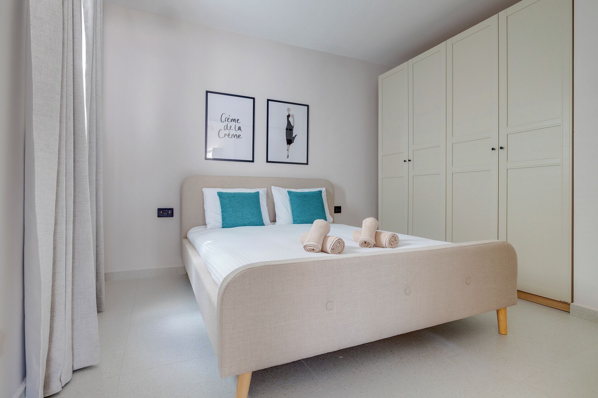 Ein Schlafzimmer mit einem Bett, zwei Kissen, einer Decke und gerollten Handtüchern. An der Wand hängen zwei gerahmte Bilder.