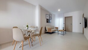 A modern living room with a dining area, a sofa, and a TV mounted on the wall.