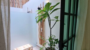 Un petit espace extérieur clos, aménagé avec un banc en bois, un pot de fleurs et un mur en bambou.