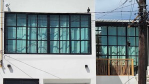 Un bâtiment moderne à deux étages, doté de grandes fenêtres, d’un balcon et d’un portail noir.
