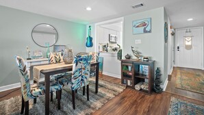 A dining area with a round mirror, a guitar, and a kitchen in the background. - Spectacular Ocean Front Bedroom Views - 626 Newhaven (Fripp Island)