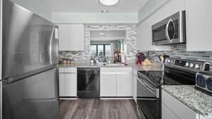 A modern kitchen with stainless steel appliances, granite countertops, and a view to the living area. - Spectacular Ocean Front Bedroom Views - 626 Newhaven (Fripp Island)