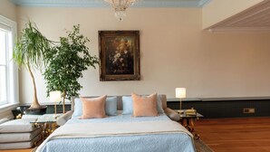 A bedroom with a large bed, a potted plant, a painting, and a chandelier. - Spacious Condo: Historic Boutique Rental in Downtown Edgerton (Edgerton)