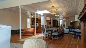 A spacious living room with a wooden dining table, multiple chairs, a sofa, and a TV displaying a movie. - Spacious Condo: Historic Boutique Rental in Downtown Edgerton (Edgerton)