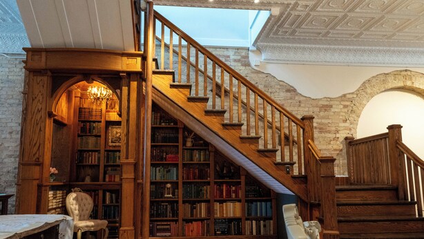 A library with wooden bookshelves, a staircase, and a chandelier. - Spacious Condo: Historic Boutique Rental in Downtown Edgerton (Edgerton)