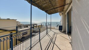 Een balkon met een metalen hekwerk, rieten dak en uitzicht op zee.