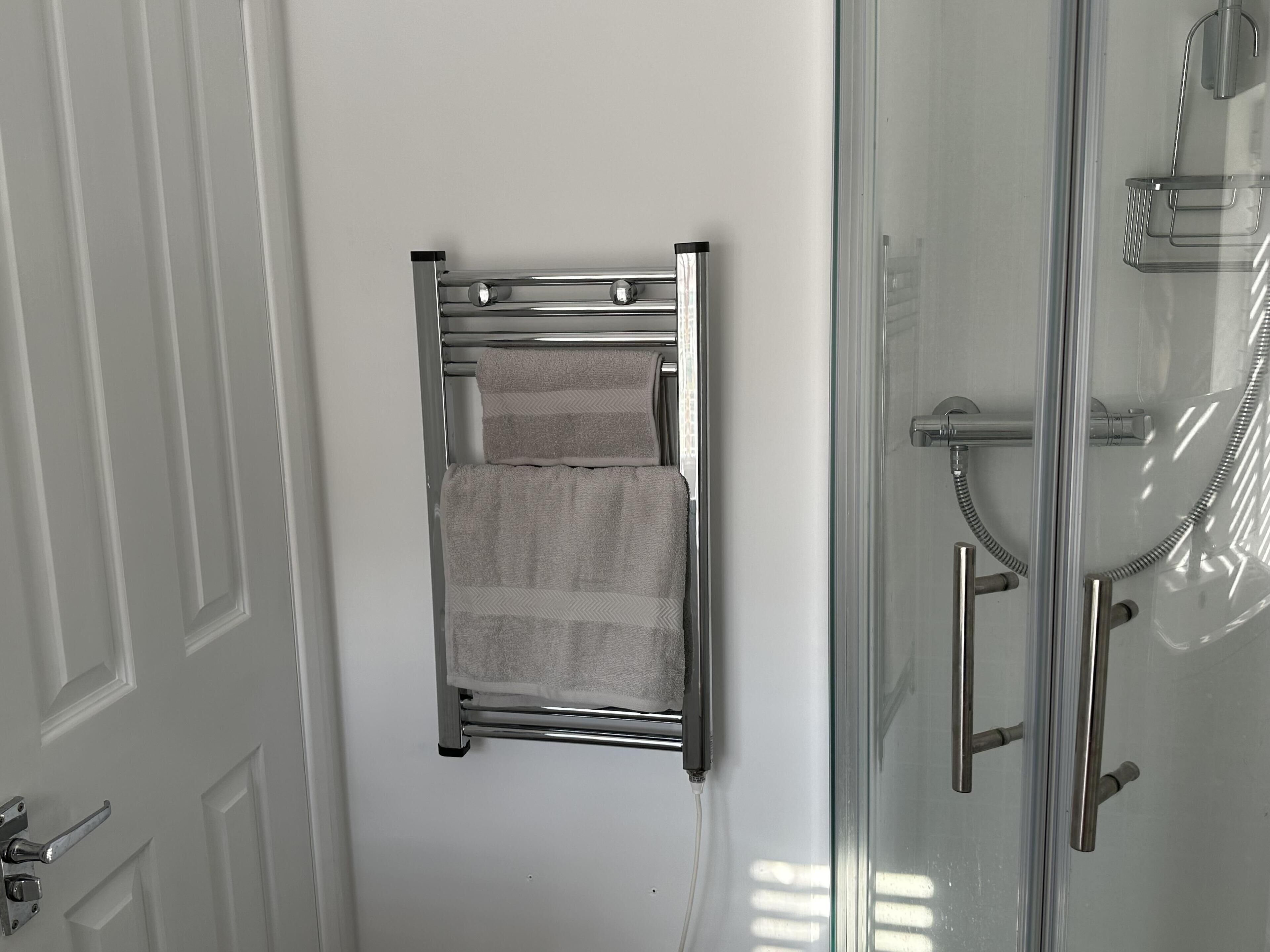 A bathroom with a towel rack, a shower, and a glass door.