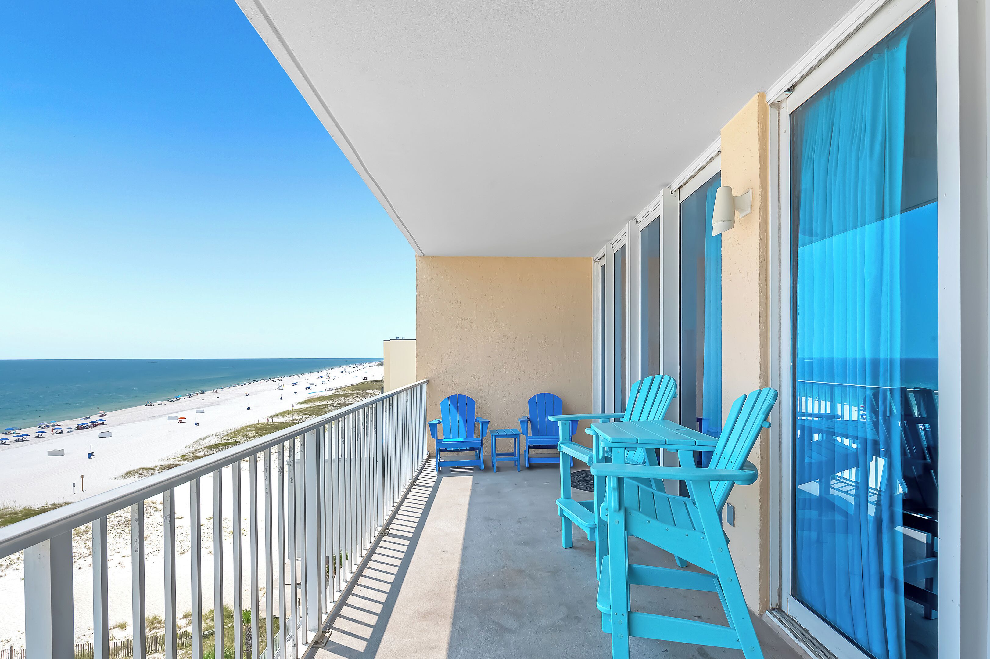 A balcony with a view of the beach, two blue chairs, and a table.