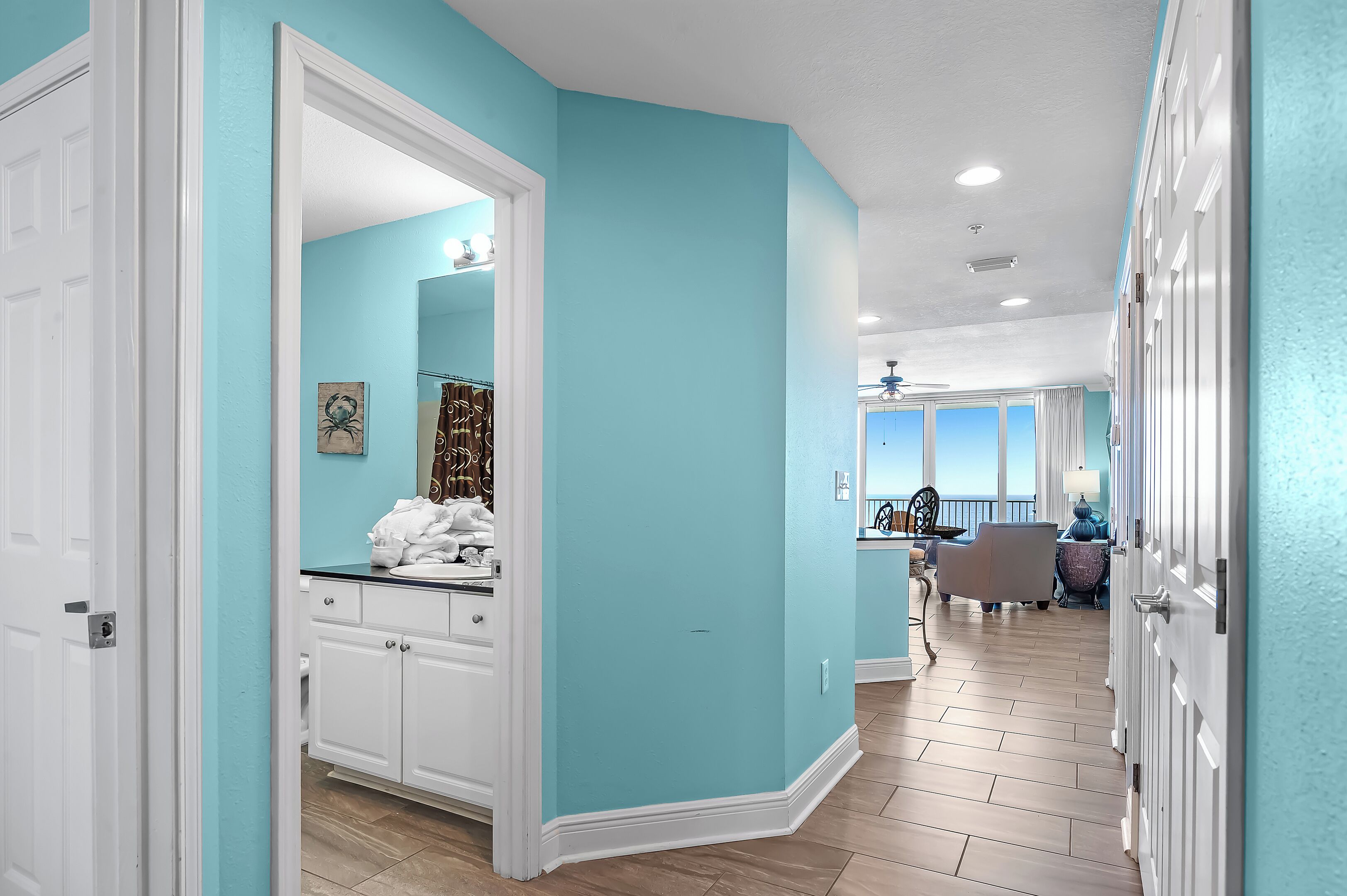 A hallway with a light blue wall, white doors, and a kitchen area visible in the background.