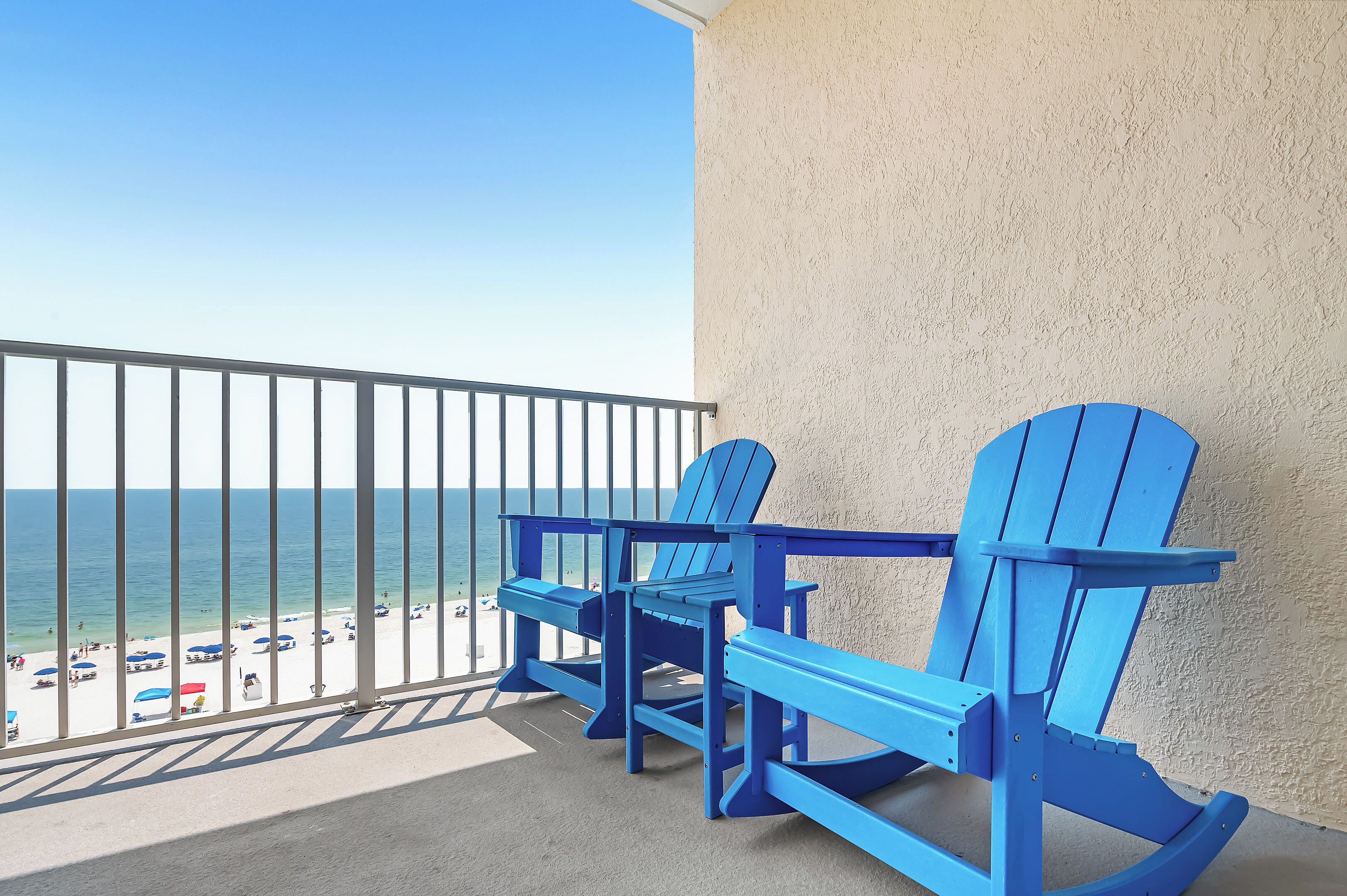 A balcony with two blue Adirondack chairs facing a beach.