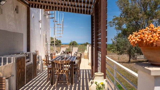 An outdoor patio with a wooden table and chairs, a grill, and a view of the sea. - Villetta Emanuela by Wonderful Italy (Syracuse)