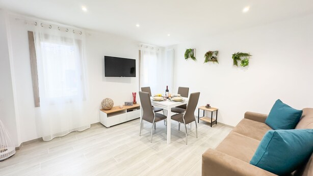 Una sala de estar moderna con comedor, un televisor de pantalla plana en la pared y un sofá beige con cojines azules.