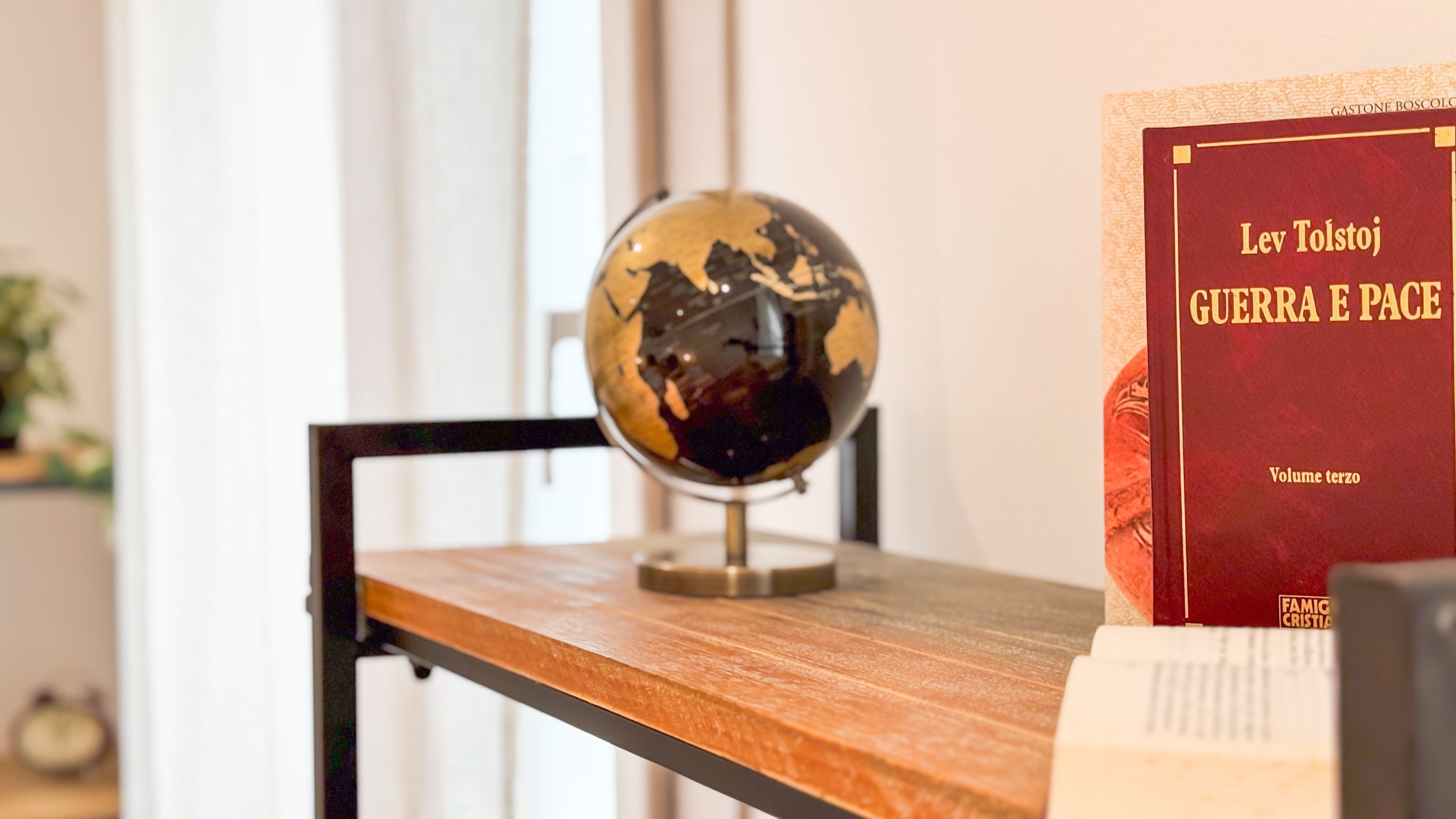 A globe on a wooden desk with a book titled 'Lev Tolstoj Guerra e Pace' on the right.