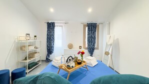 Une chambre d’hôtel avec un lit, une petite table avec des serviettes et des articles de toilette, une étagère avec des boîtes de rangement et une fenêtre avec des rideaux.
