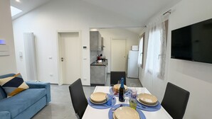 Un salon moderne avec un canapé bleu, une table à manger dressée avec des assiettes, des verres et des couverts, et une cuisine en arrière-plan.
