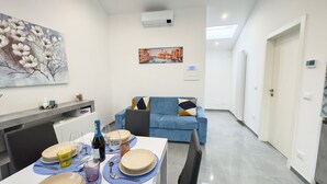 Un salon moderne avec un canapé bleu, une table à manger dressée pour quatre personnes et un tableau représentant un paysage urbain.
