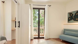 A room with a wooden floor, a blue sofa, a large window with curtains, and a painting on the wall. - La Riera Principal (Barcelona)