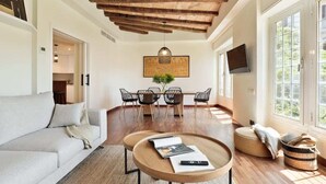 A spacious living area with a wooden ceiling, a sofa, a coffee table, a dining table with chairs, and a television on the wall. - La Riera Principal (Barcelona)