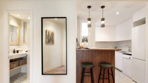 A modern kitchen with white cabinets, a wooden island, two bar stools, and pendant lights. - La Riera Principal (Barcelona)