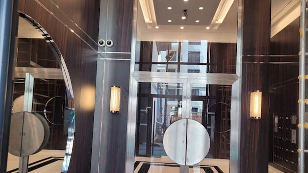 Un hall d’ascenseur moderne avec une porte en verre, des éléments décoratifs métalliques et un motif géométrique sur le sol.