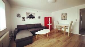 A modern living room with a sectional sofa, a dining table with chairs, a red refrigerator, and wall art including a famous bridge. - Cozy Holeby Pet-friendly Villa - Puttgarden/fermen/lalandia/knuthenborg (Holeby)