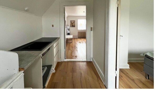A narrow hallway with a kitchen area on the left, a door leading to a bedroom on the right, and a view into a living room with a window. - Cozy Holeby Pet-friendly Villa - Puttgarden/fermen/lalandia/knuthenborg (Holeby)