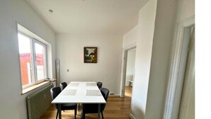 A room with a white table and four chairs, a radiator, a window, and a painting on the wall. - Cozy Holeby Pet-friendly Villa - Puttgarden/fermen/lalandia/knuthenborg (Holeby)