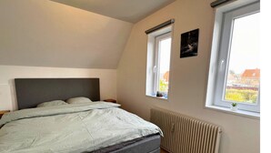 A bedroom with a bed, a radiator, and two windows with views of the outside. - Cozy Holeby Pet-friendly Villa - Puttgarden/fermen/lalandia/knuthenborg (Holeby)