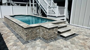 A rectangular swimming pool with stone steps leading into it, surrounded by a stone wall and a paved patio. - SEA BISCUIT-2024 LUXURY Cherry Grove Home, 4bd/3bth, Private Pool, VERY CLEAN (North Myrtle Beach)