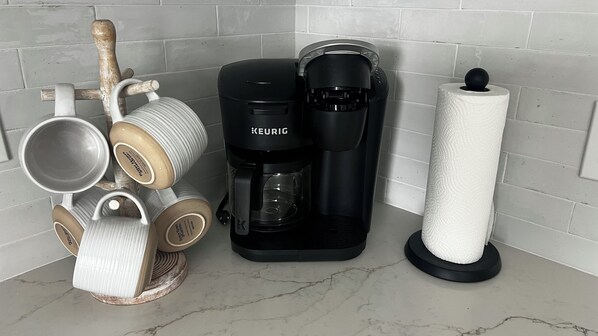 A coffee maker, a stack of mugs, and a roll of paper towels on a kitchen counter.