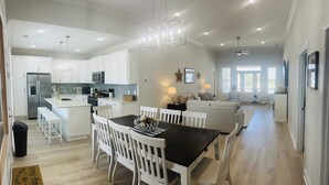 A spacious kitchen with white cabinetry, a central island, and a dining area with white chairs. - SEA BISCUIT-2024 LUXURY Cherry Grove Home, 4bd/3bth, Private Pool, VERY CLEAN (North Myrtle Beach)