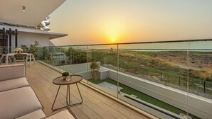 Ein moderner Balkon mit Glastrennwand, der einen Blick auf den Sonnenuntergang über eine grüne Landschaft bietet.