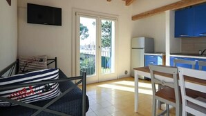Una habitación con cama, televisión montada en la pared, mesa de comedor con sillas y una zona de cocina con armarios azules.