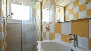 Un baño con cabina de ducha de vidrio, un lavamanos blanco y azulejos blancos y amarillos a cuadros.