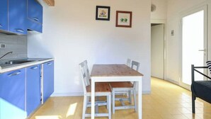 Una cocina funcional con armarios azules, una mesa de madera con cuatro sillas y dos cuadros en la pared.