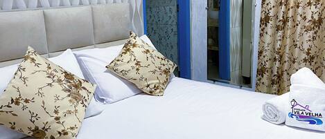 A hotel room with a bed, two floral-patterned pillows, a rolled towel, and a shower area with a blue door.
