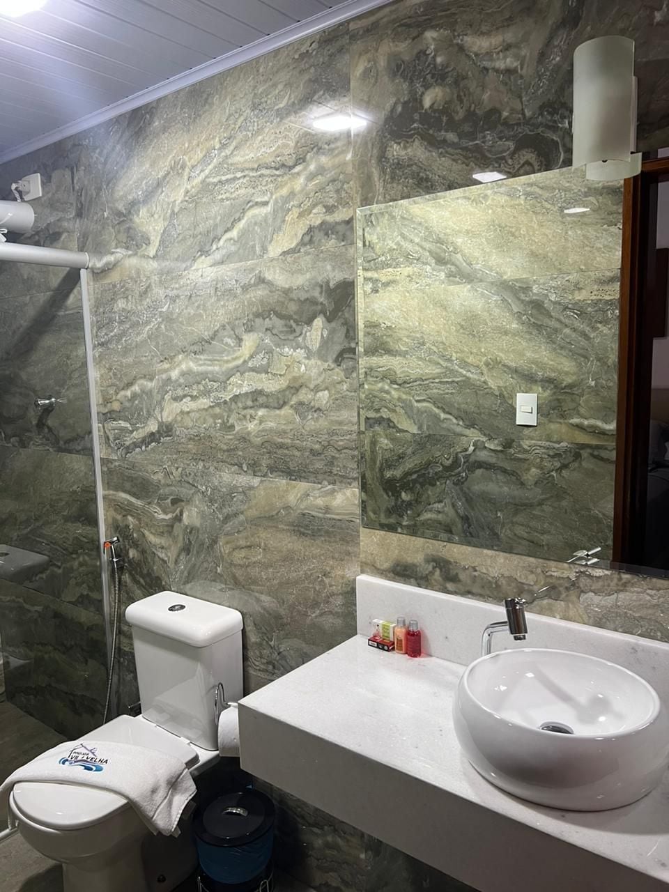 A bathroom with a marble wall, a toilet, a sink, and a mirror.