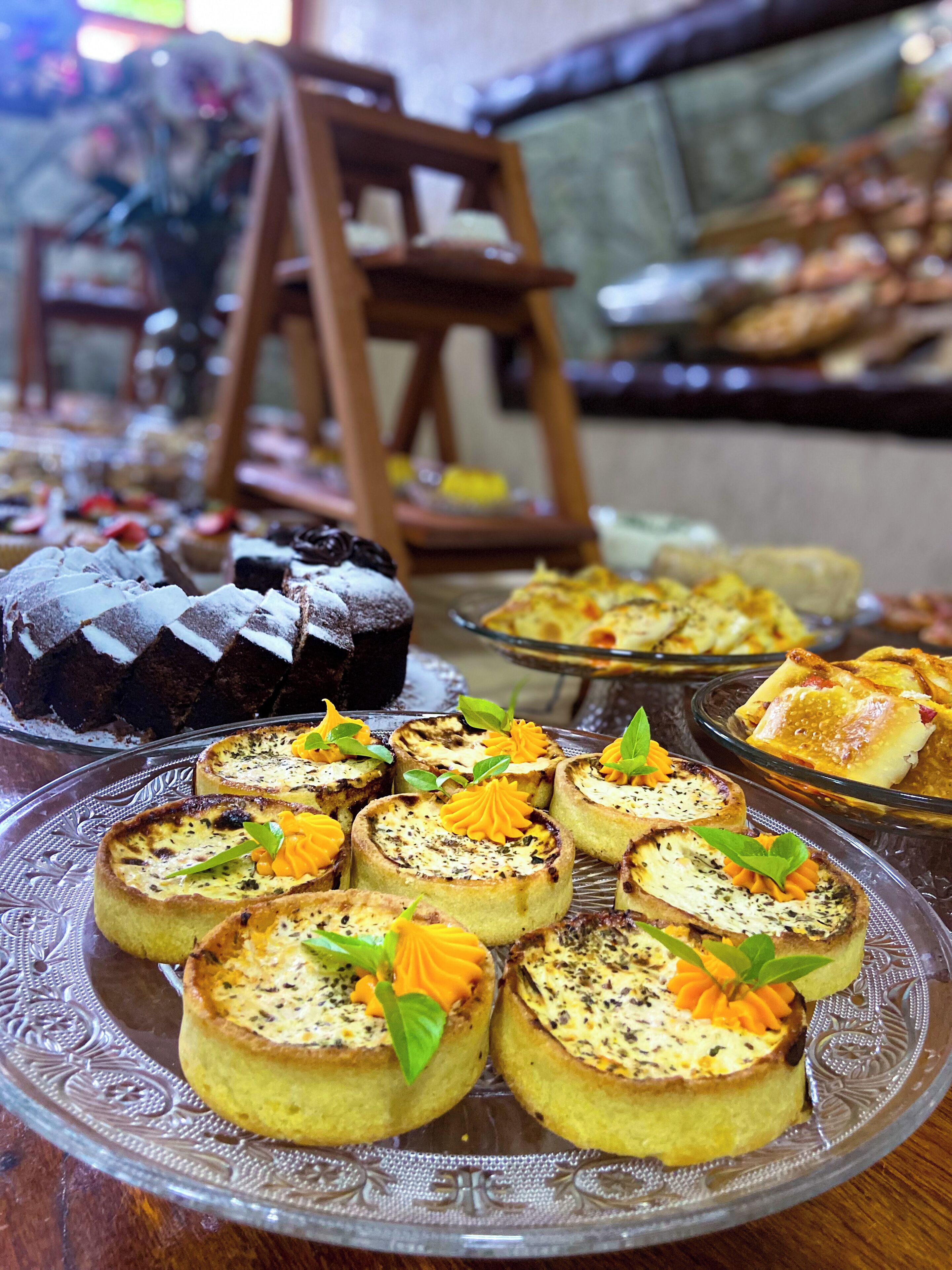 Verschiedene Desserts auf einer Glasplatte, darunter kleine Törtchen und ein Kuchen, mit einem Holzstuhl und einer Glasvitrine im Hintergrund.