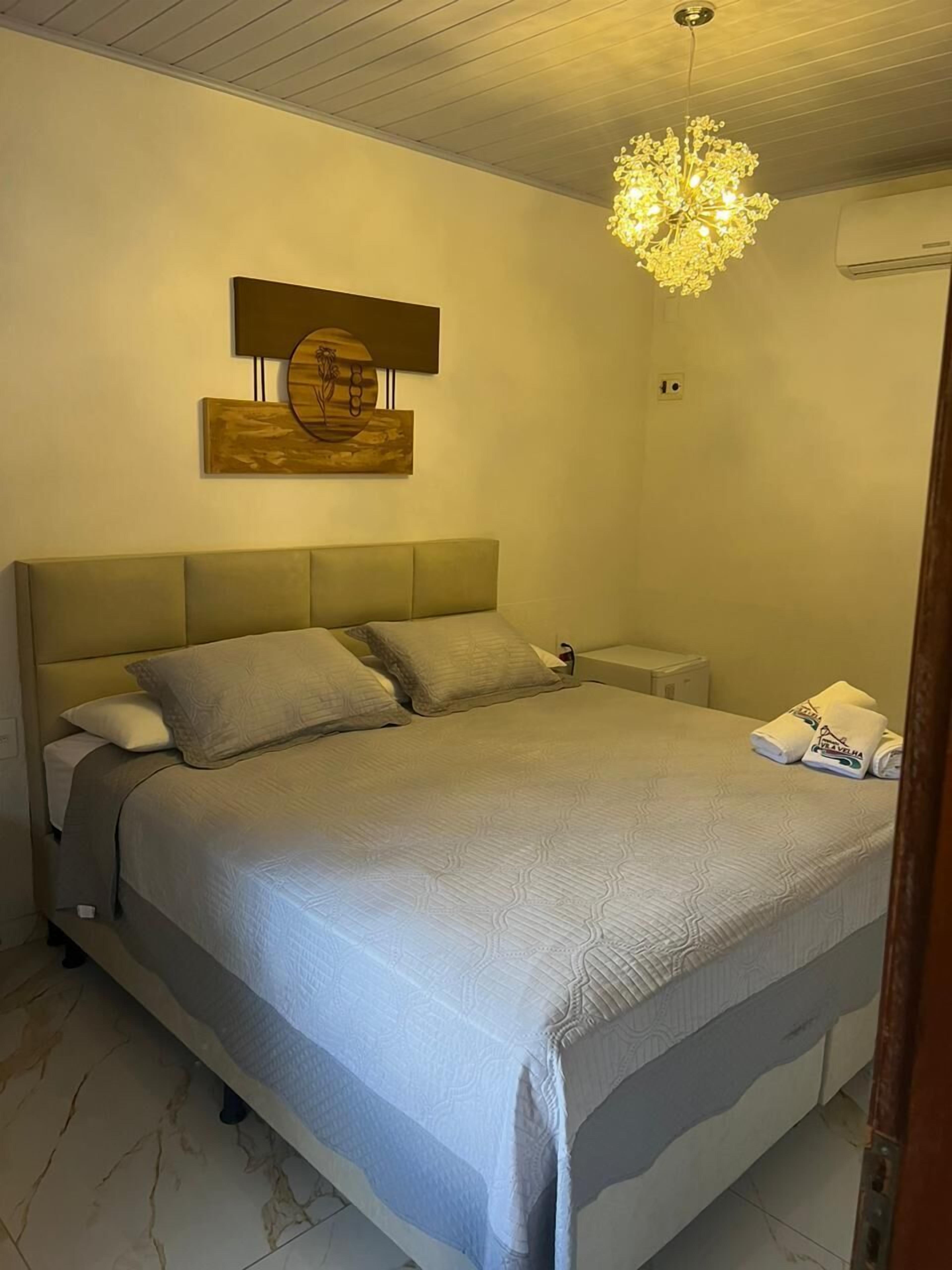A bedroom with a bed, bedside tables, a chandelier, and artwork on the wall.